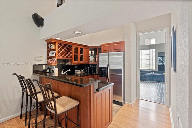 kitchen with light hardwood / wood-style floors, stainless steel fridge with ice dispenser, a kitchen breakfast bar, and kitchen peninsula