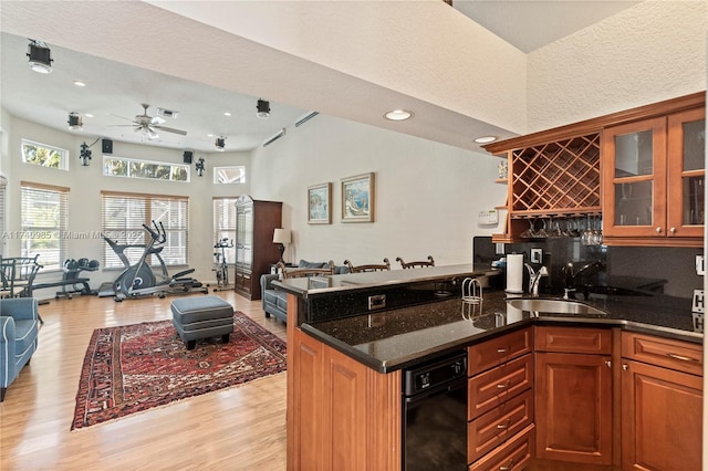 kitchen featuring sink, light hardwood / wood-style flooring, ceiling fan, dark stone countertops, and kitchen peninsula