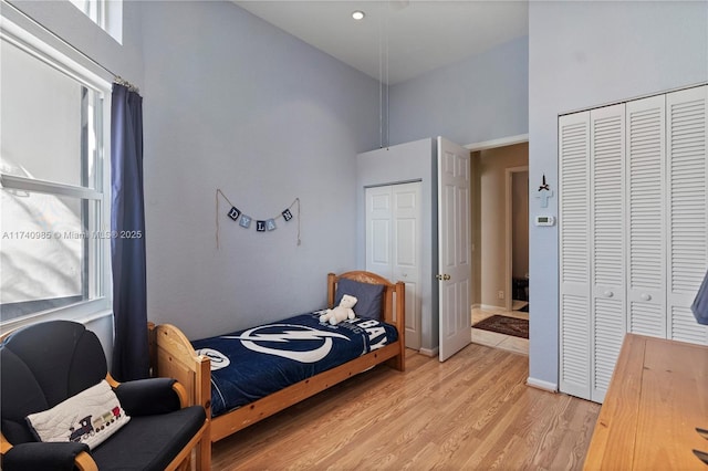 bedroom featuring multiple windows, a towering ceiling, and light hardwood / wood-style floors