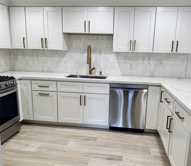 kitchen with white cabinetry, stainless steel appliances, sink, and light stone counters