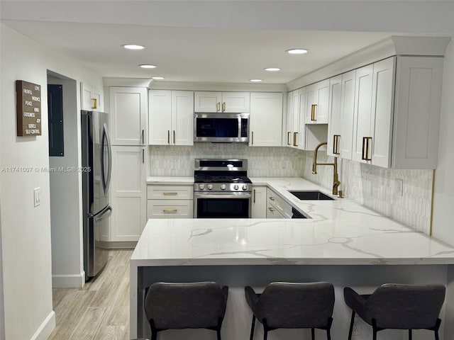 kitchen with sink, white cabinetry, stainless steel appliances, a kitchen breakfast bar, and kitchen peninsula