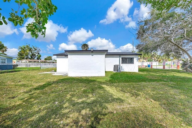 rear view of property featuring central AC and a lawn