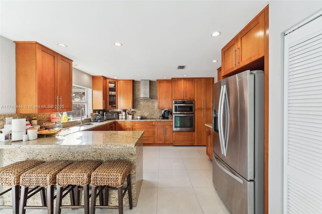 kitchen featuring a kitchen bar, appliances with stainless steel finishes, kitchen peninsula, wall chimney range hood, and backsplash