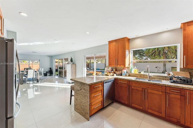 kitchen with sink, backsplash, stainless steel appliances, light stone countertops, and kitchen peninsula