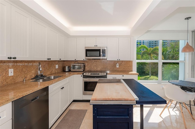 kitchen featuring sink, light stone counters, decorative light fixtures, appliances with stainless steel finishes, and white cabinets