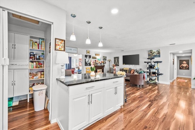 kitchen featuring pendant lighting, dark stone counters, light hardwood / wood-style flooring, and white cabinets