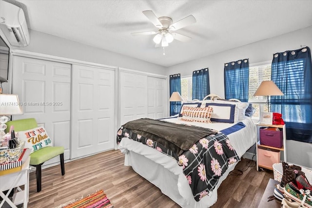 bedroom with hardwood / wood-style flooring, a textured ceiling, a wall unit AC, and two closets