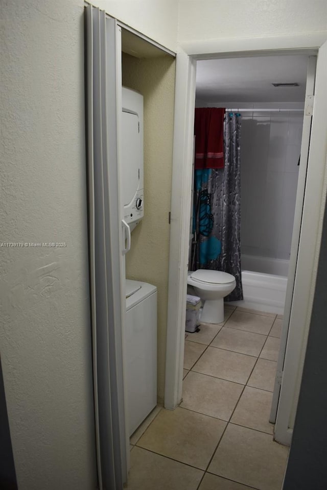 bathroom with tile patterned floors, stacked washer and clothes dryer, toilet, and shower / tub combo