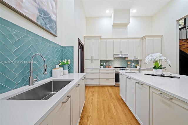 kitchen with sink, decorative backsplash, light hardwood / wood-style floors, and stainless steel range oven