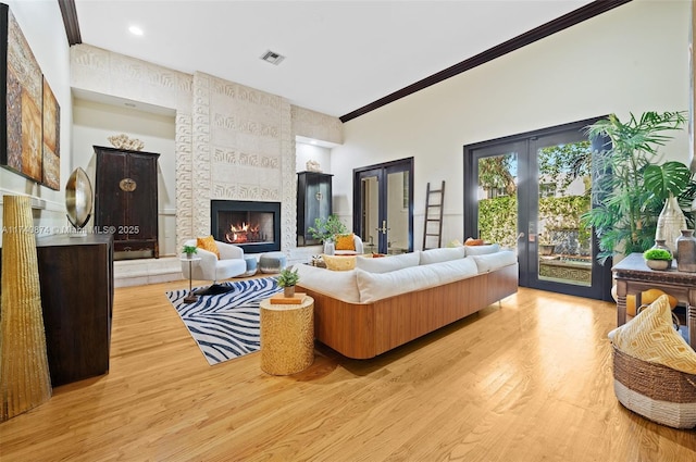 living room featuring french doors, a large fireplace, crown molding, and light hardwood / wood-style flooring