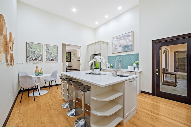 kitchen featuring white cabinetry, sink, backsplash, a center island with sink, and light wood-type flooring