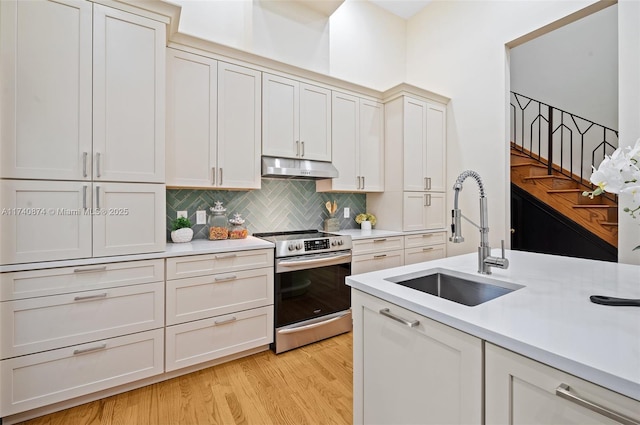 kitchen featuring white cabinetry, sink, backsplash, stainless steel range with electric stovetop, and light wood-type flooring