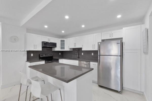 kitchen with sink, a kitchen breakfast bar, stainless steel appliances, decorative backsplash, and white cabinets