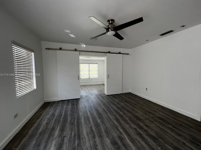 spare room featuring dark hardwood / wood-style flooring, a barn door, and ceiling fan