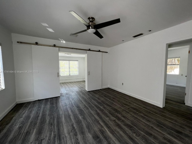 unfurnished room with dark wood-type flooring, ceiling fan, and a barn door