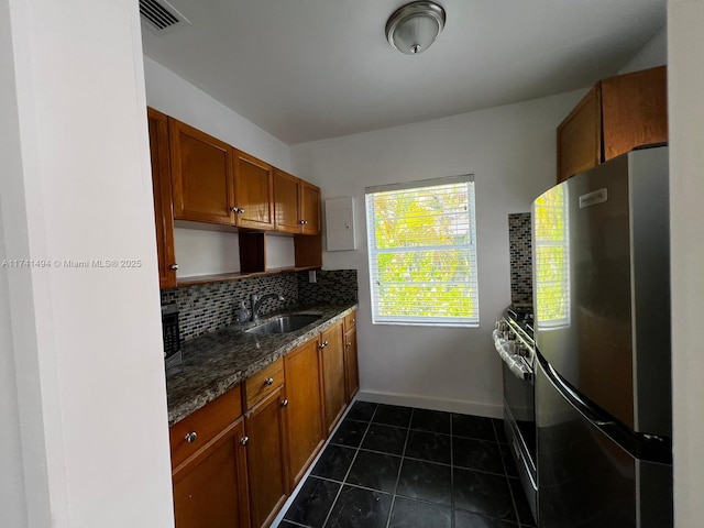 kitchen with stainless steel refrigerator, range with gas cooktop, tasteful backsplash, sink, and dark tile patterned flooring