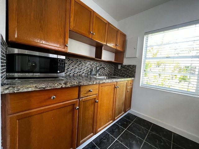 kitchen featuring tasteful backsplash, dark stone counters, dark tile patterned flooring, and sink