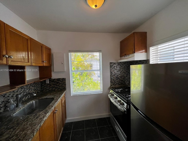 kitchen featuring appliances with stainless steel finishes, sink, decorative backsplash, dark tile patterned floors, and dark stone counters