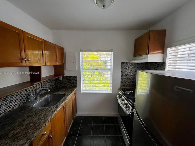 kitchen with appliances with stainless steel finishes, sink, dark stone countertops, backsplash, and dark tile patterned floors