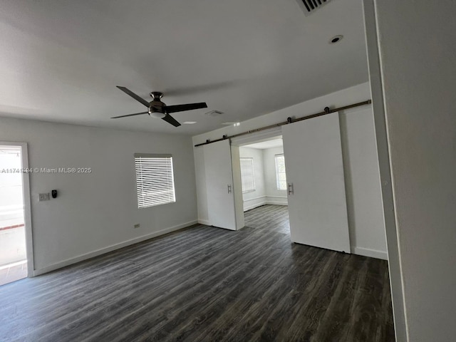 unfurnished room featuring dark hardwood / wood-style floors, a barn door, and ceiling fan