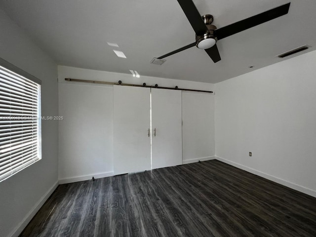 spare room with dark hardwood / wood-style flooring, a barn door, and ceiling fan