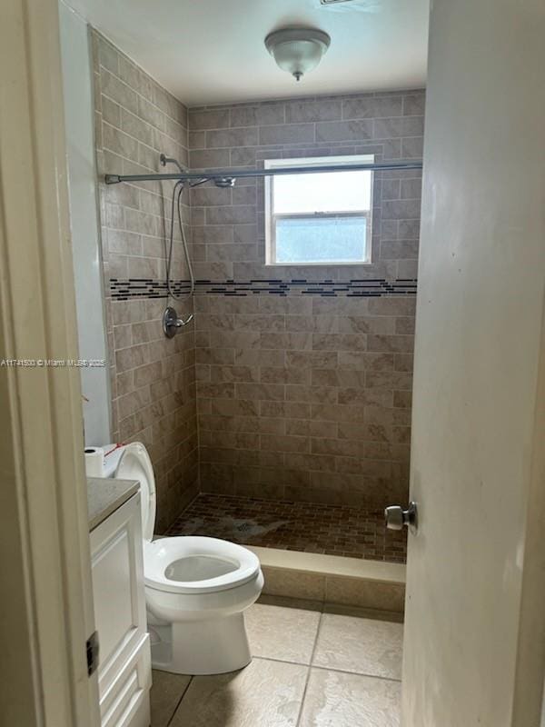 bathroom featuring vanity, tile patterned flooring, toilet, and tiled shower