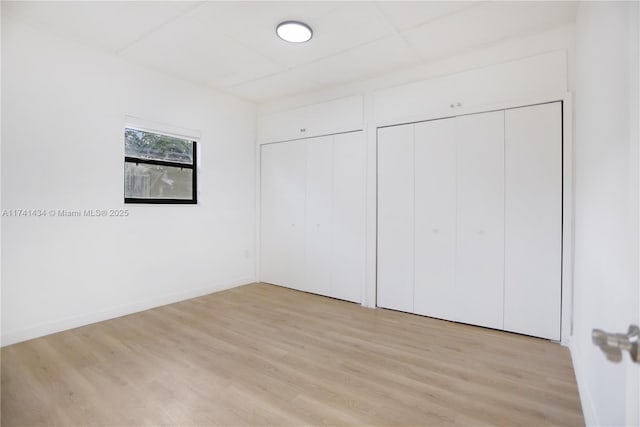 unfurnished bedroom with a drop ceiling, light wood-type flooring, and two closets