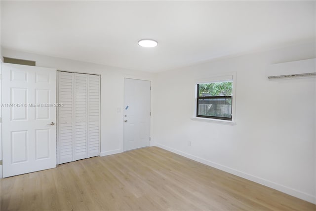 unfurnished bedroom with a wall mounted air conditioner, light wood-type flooring, and a closet