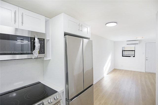 kitchen with light hardwood / wood-style floors, a wall mounted AC, white cabinets, and appliances with stainless steel finishes