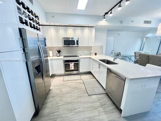 kitchen with sink, white cabinets, decorative backsplash, kitchen peninsula, and stainless steel appliances