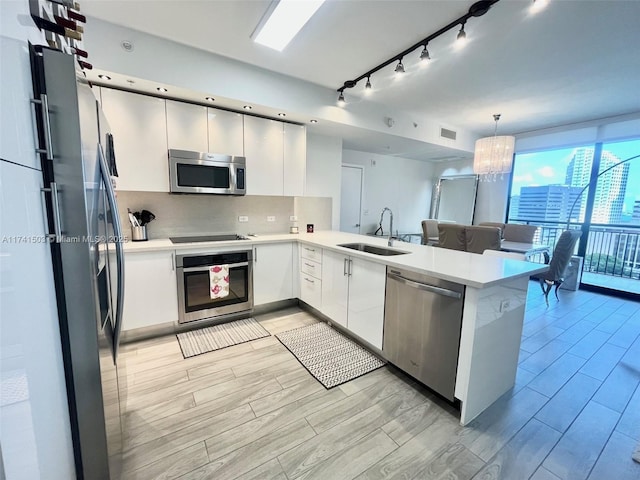 kitchen featuring sink, backsplash, hanging light fixtures, kitchen peninsula, and stainless steel appliances