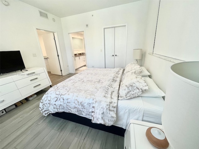 bedroom with ensuite bath, light wood-type flooring, and a closet