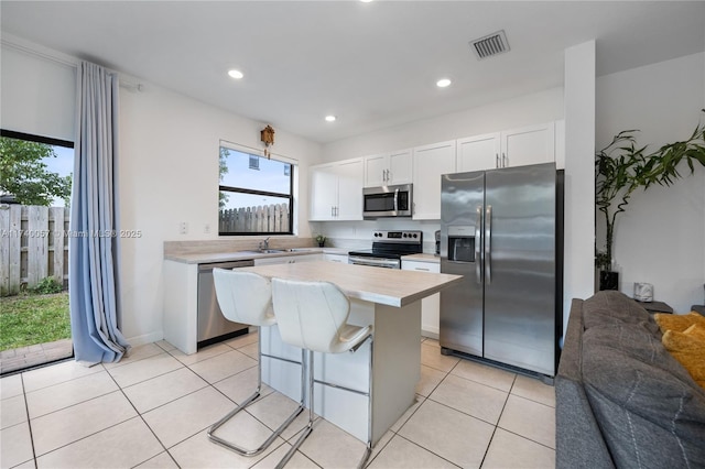 kitchen featuring a kitchen island, appliances with stainless steel finishes, white cabinetry, a kitchen bar, and light tile patterned floors