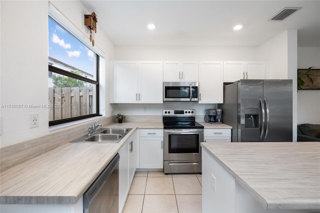 kitchen featuring sink, light tile patterned floors, stainless steel appliances, and white cabinets