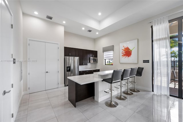 kitchen with dark brown cabinetry, a breakfast bar area, a center island, appliances with stainless steel finishes, and a high ceiling