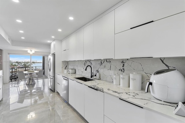 kitchen with appliances with stainless steel finishes, tasteful backsplash, white cabinetry, sink, and light stone countertops