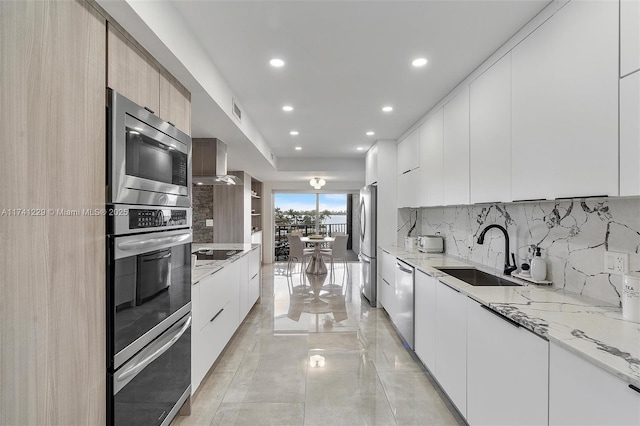 kitchen with sink, wall chimney range hood, stainless steel appliances, and white cabinets
