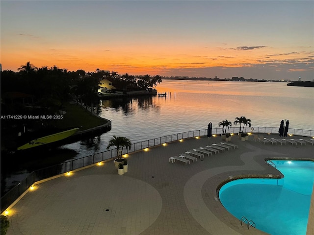 pool at dusk featuring a patio and a water view