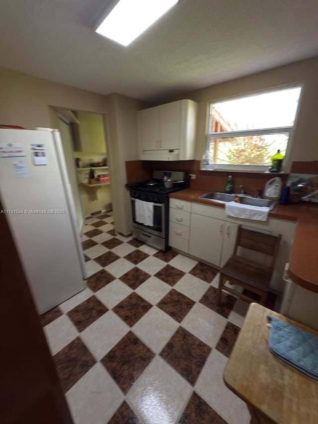 kitchen with dark floors, freestanding refrigerator, stainless steel gas range, under cabinet range hood, and a sink