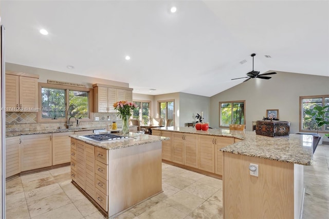 kitchen with sink, a kitchen island, light stone countertops, light brown cabinets, and stainless steel gas cooktop