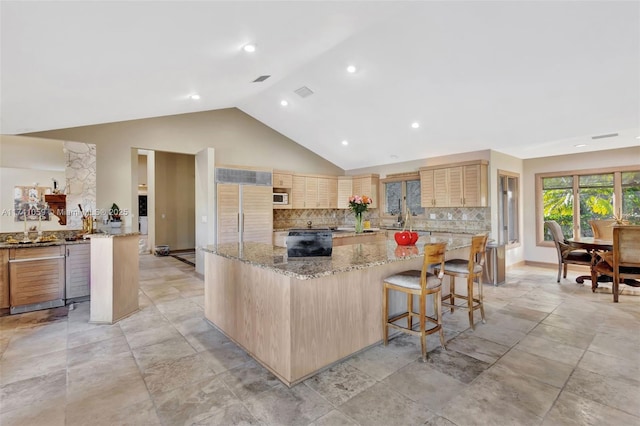 kitchen featuring tasteful backsplash, a breakfast bar area, light stone countertops, paneled built in fridge, and a kitchen island