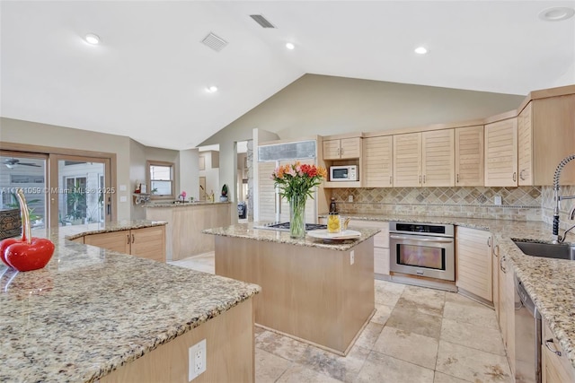 kitchen with sink, a kitchen island, stainless steel appliances, light brown cabinets, and light stone countertops