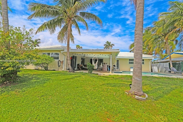 rear view of house with stucco siding, a lawn, a patio area, fence, and an outdoor pool