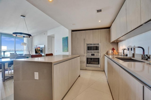 kitchen with a kitchen island, appliances with stainless steel finishes, light brown cabinetry, sink, and light tile patterned floors