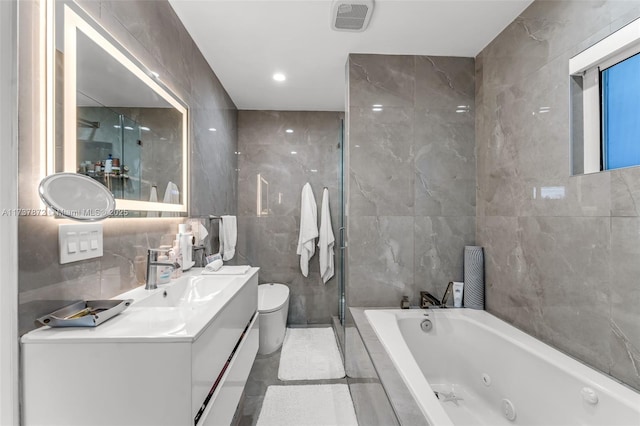 bathroom with toilet, visible vents, vanity, tile walls, and a whirlpool tub