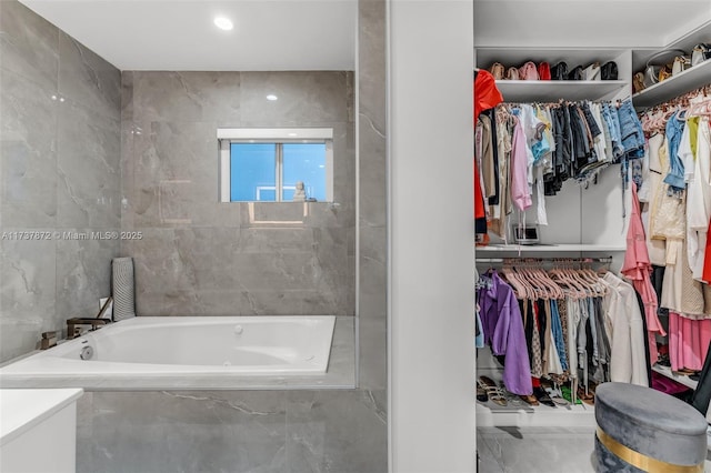 bathroom featuring marble finish floor, a spacious closet, a tub with marble appearance, and tile walls