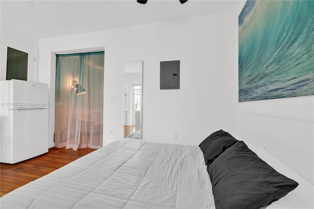 bedroom featuring white refrigerator, hardwood / wood-style floors, electric panel, and ceiling fan