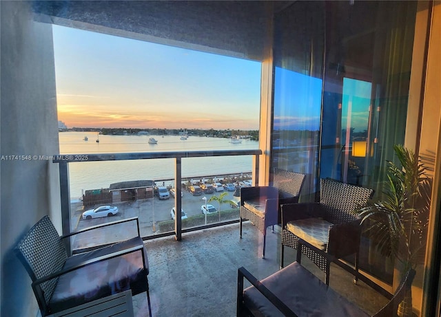 balcony at dusk featuring a water view