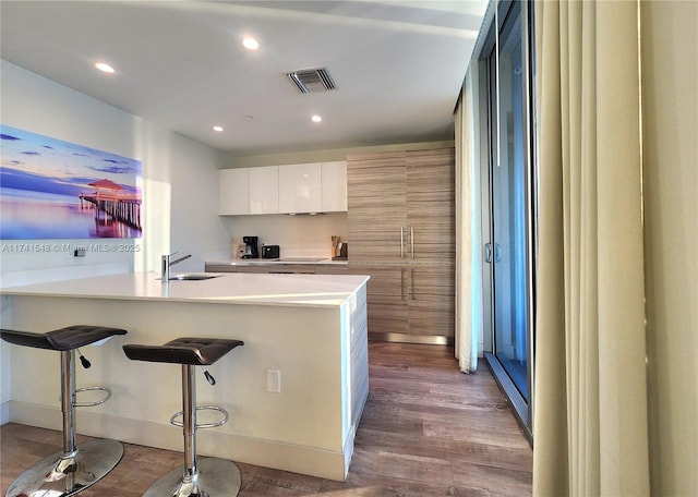 kitchen with sink, a breakfast bar area, light hardwood / wood-style floors, white cabinets, and black electric cooktop