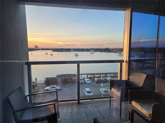 balcony at dusk featuring a water view